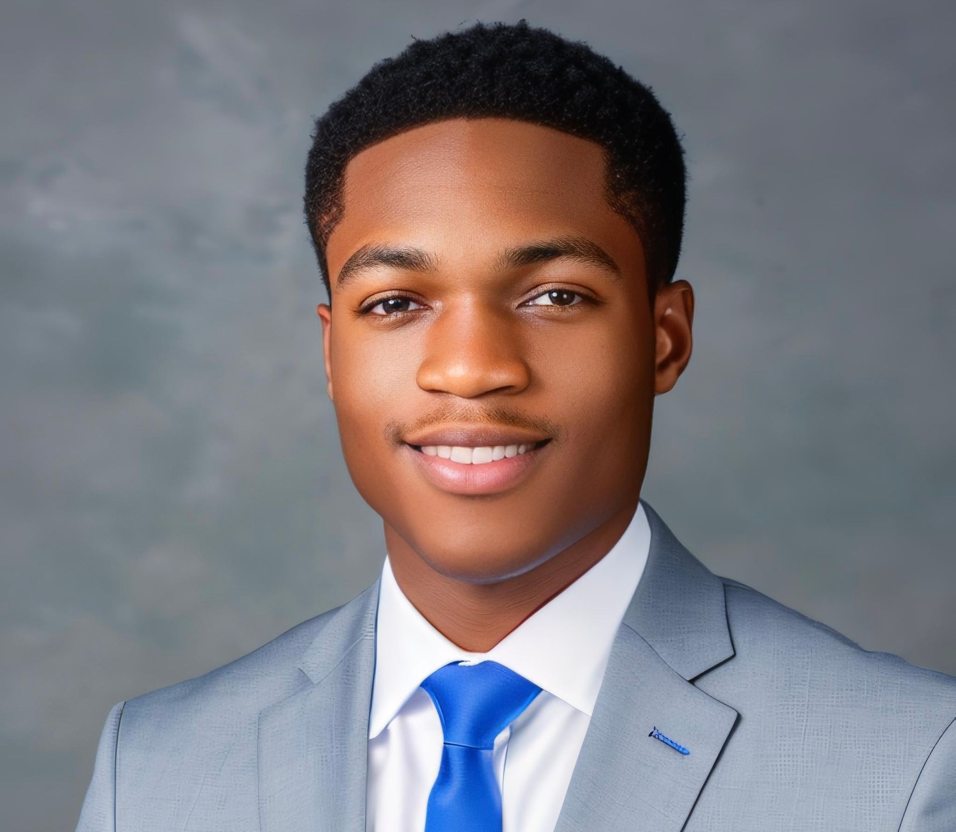 Person wearing a light gray suit with a blue tie against a gray background.